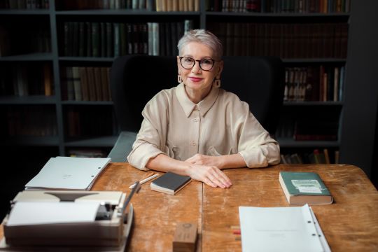 Smart Elderly Lady Sitting At Desk In Home Library